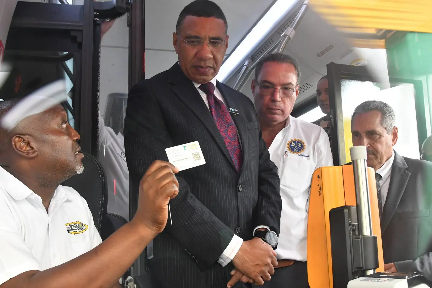 Adrian Walker (left) shows Prime MInister Andrew Holness (centre) and Transport Minister Daryl Vaz the new JUTC card during the handover of 100 new buses to the State-owned company on Tuesday.